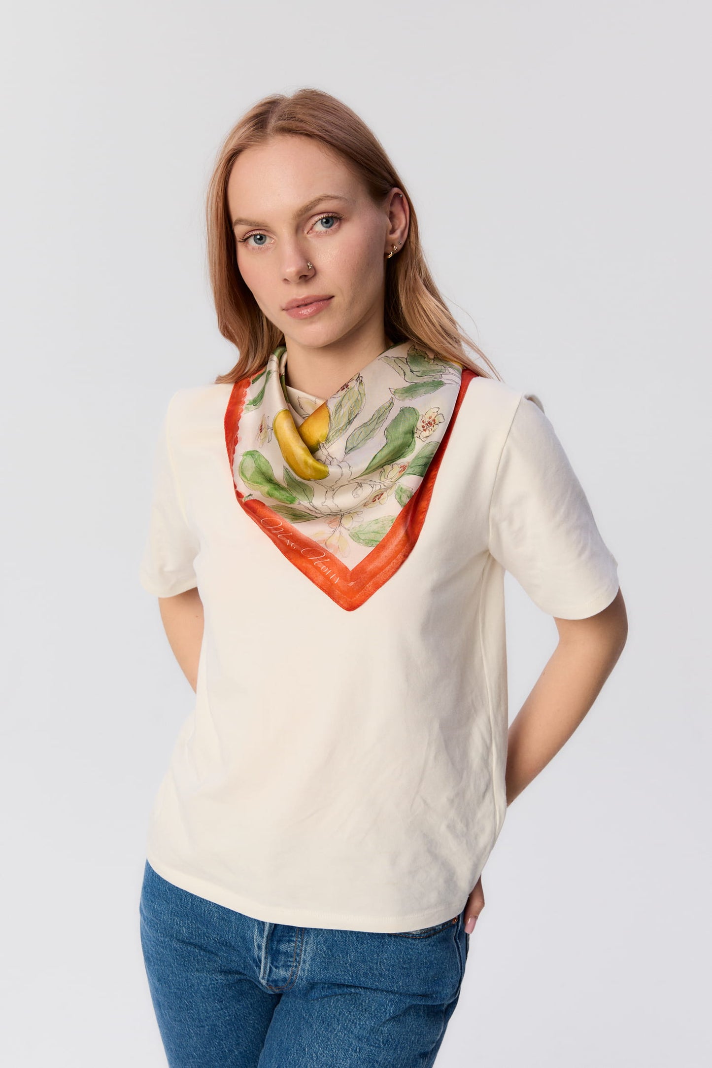 Modelka w kremowym T-shircie i jeansach, z apaszką MAG NOLLY w print gruszek zawiązaną na szyi.