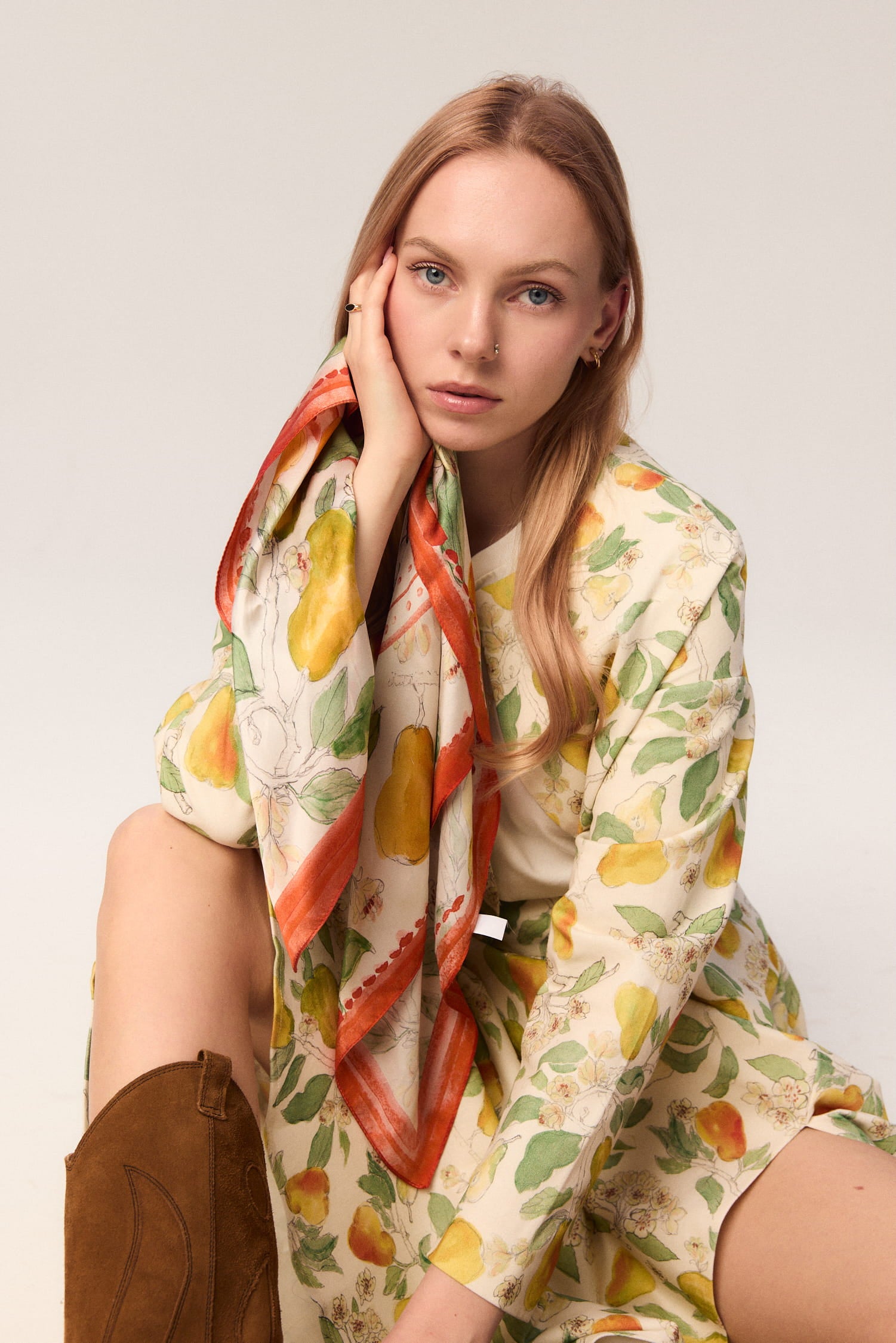 Modelka siedząca w stylizacji MAG NOLLY z apaszką w print gruszek owiniętą wokół ramienia.