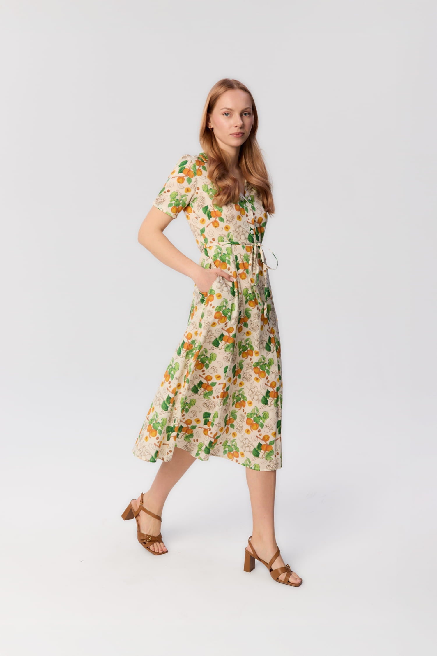 Modelka w sukience Bellucci z printem moreli – widok z profilu, sukienka midi z kołnierzykiem, paskiem i kieszeniami, letnia stylizacja w ruchu