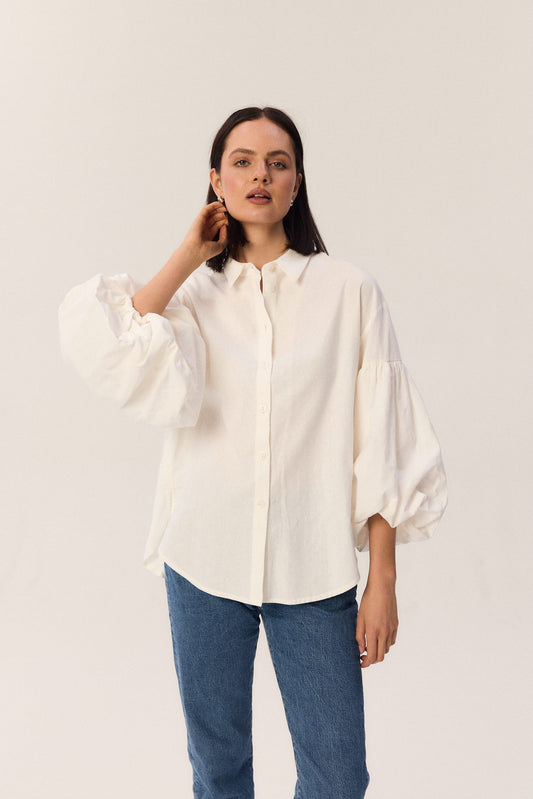 Modelka w kremowej koszuli Lisi z bufiastymi rękawami, zdjęcie z kampanii na beżowym tle.