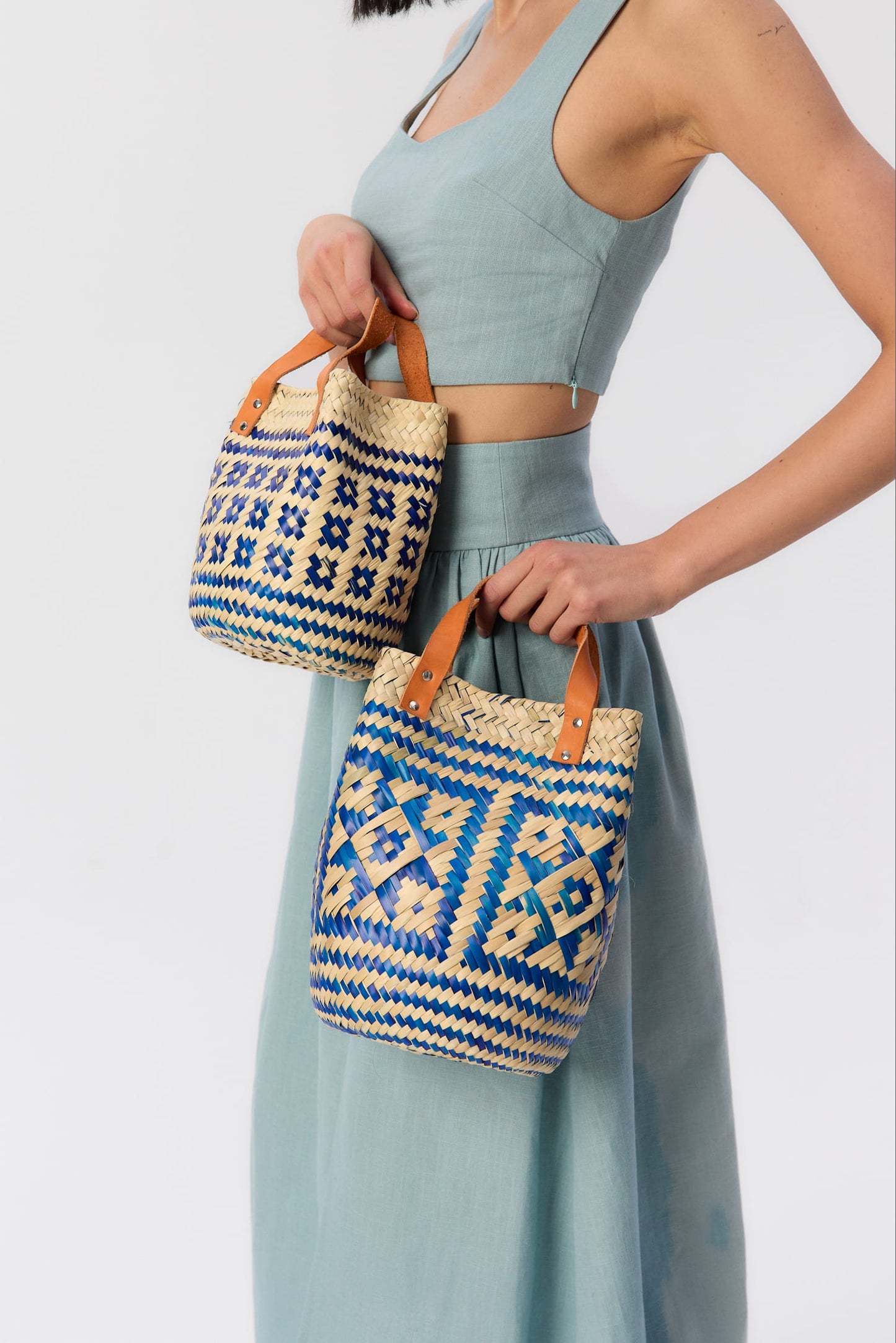 Modelka z dwoma plecionymi koszykami Vitti (mini i small) w odcieniach niebieskiego – ręcznie robione dodatki z liści palmowych i skórzanymi rączkami, w stylu boho.