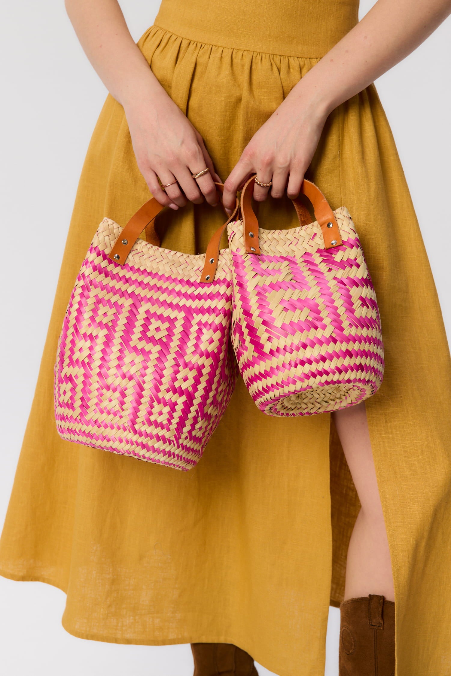 Modelka trzyma dwa plecione koszyki Vitti w odcieniach różu – ręcznie wykonane z liści palmowych, z rączkami ze skóry naturalnej, w stylu boho.
