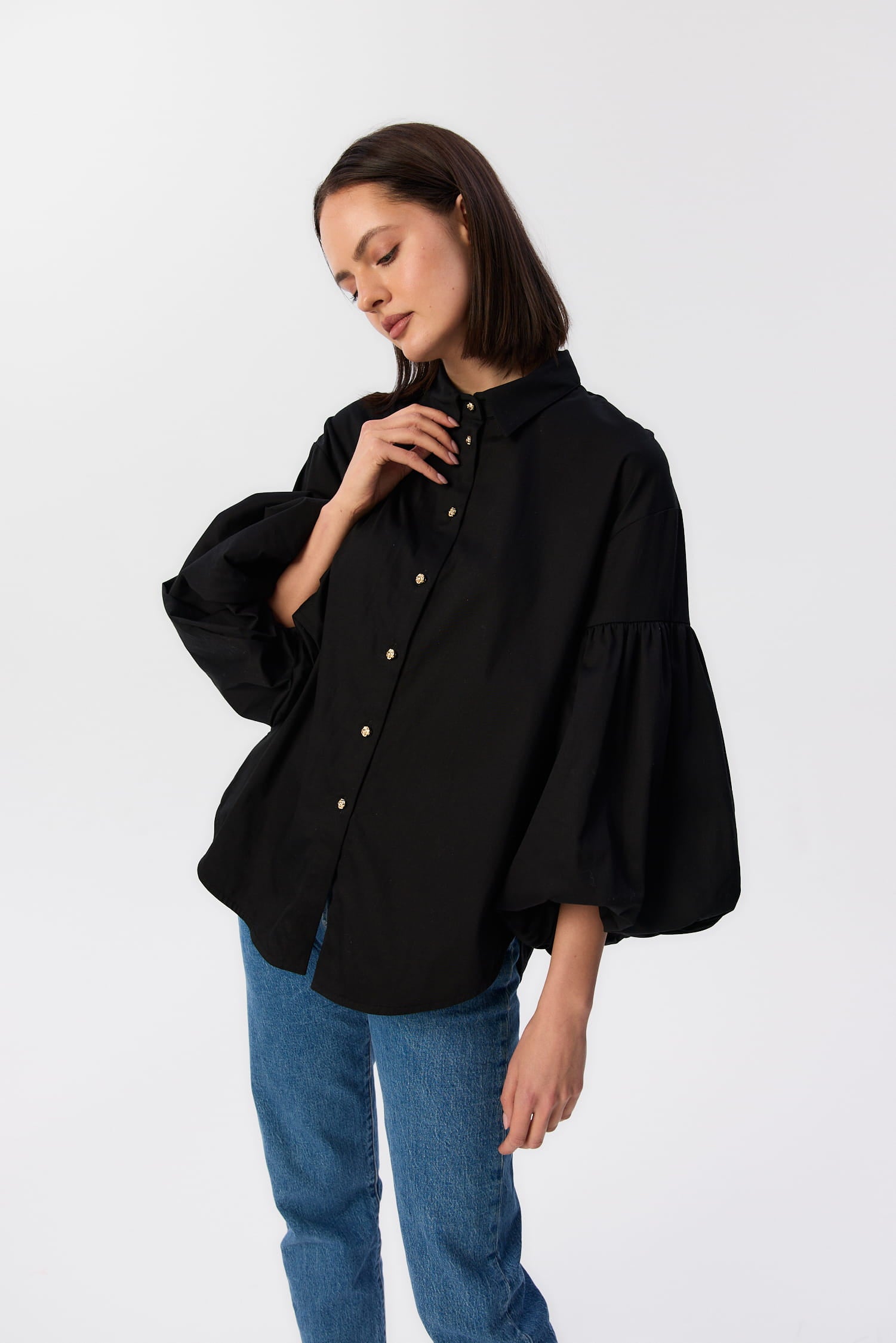 Czarna koszula Lisi MAG NOLLY z bufiastymi rękawami i złotymi guzikami, modelka w jeansach trzyma kołnierzyk.