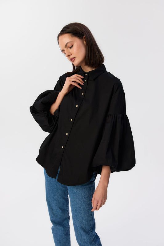 Czarna koszula Lisi MAG NOLLY z bufiastymi rękawami i złotymi guzikami, modelka w jeansach trzyma kołnierzyk.