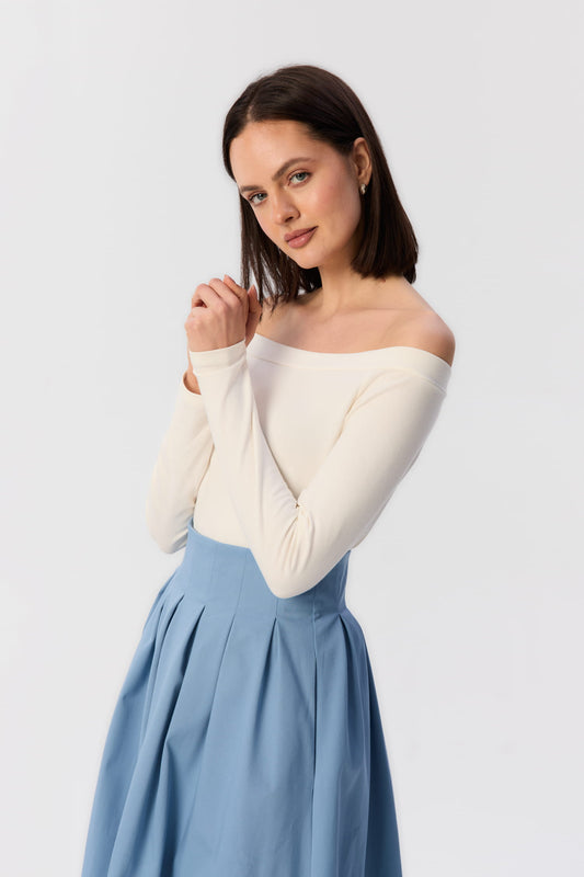 Modelka w kremowym longsleeve’ie Mori z certyfikowanej bawełny, z dekoltem na ramiona i spódnicą midi w kolorze niebieskim – MAG NOLLY.