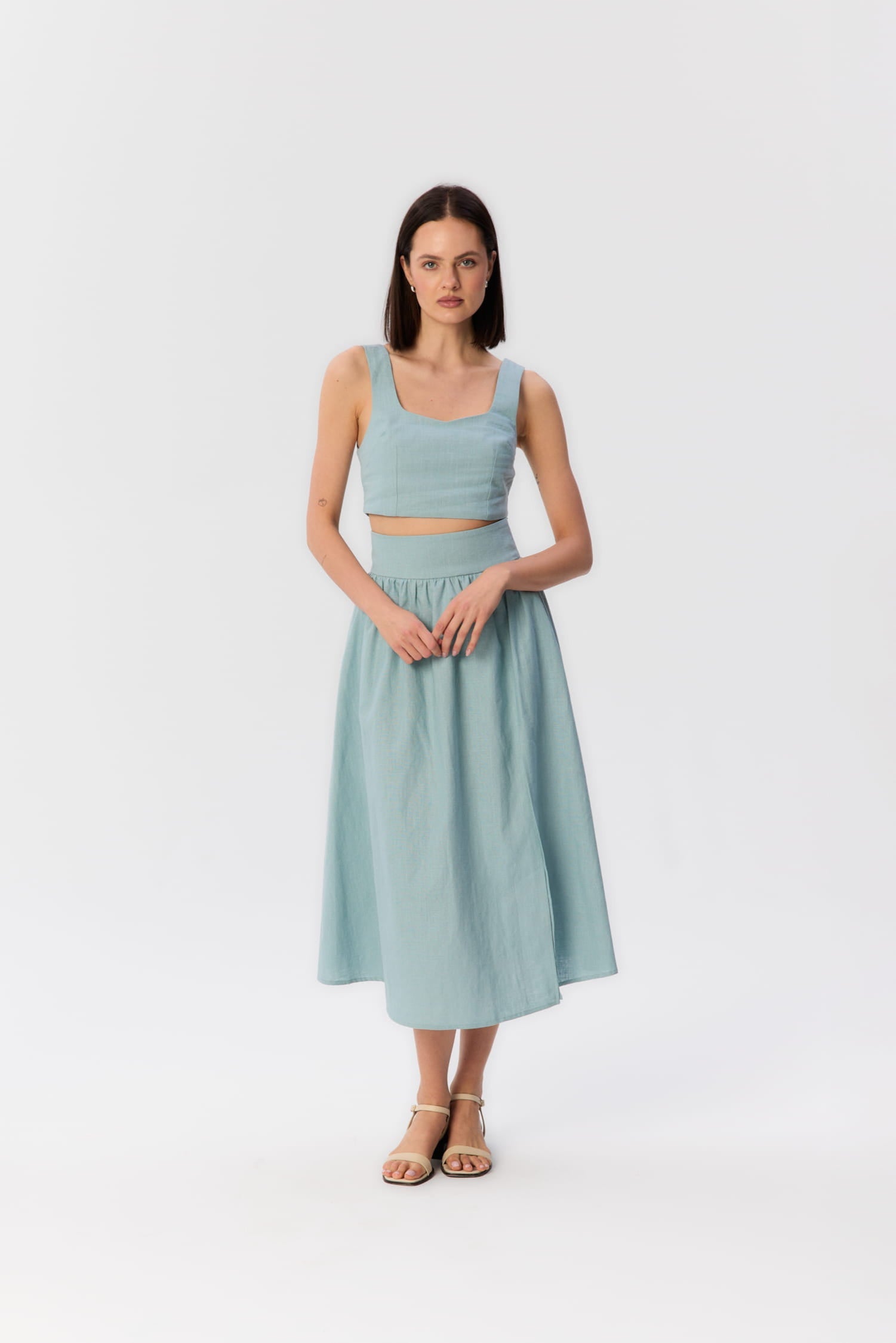 Modelka w turkusowym komplecie z topem i spódnicą midi z wysokim stanem, widok z przodu.