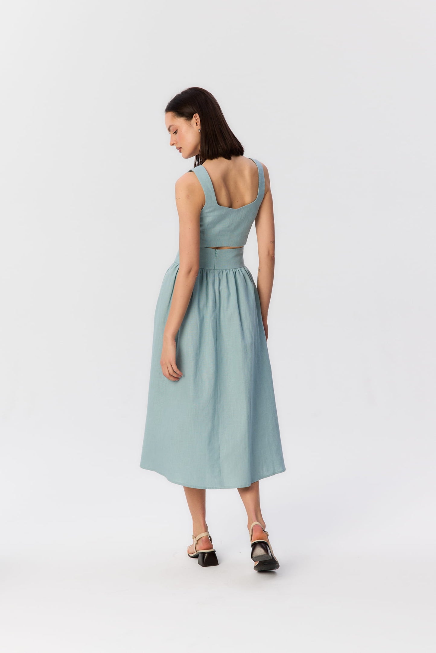 Modelka tyłem w turkusowym komplecie z topem i spódnicą midi z wysokim stanem.