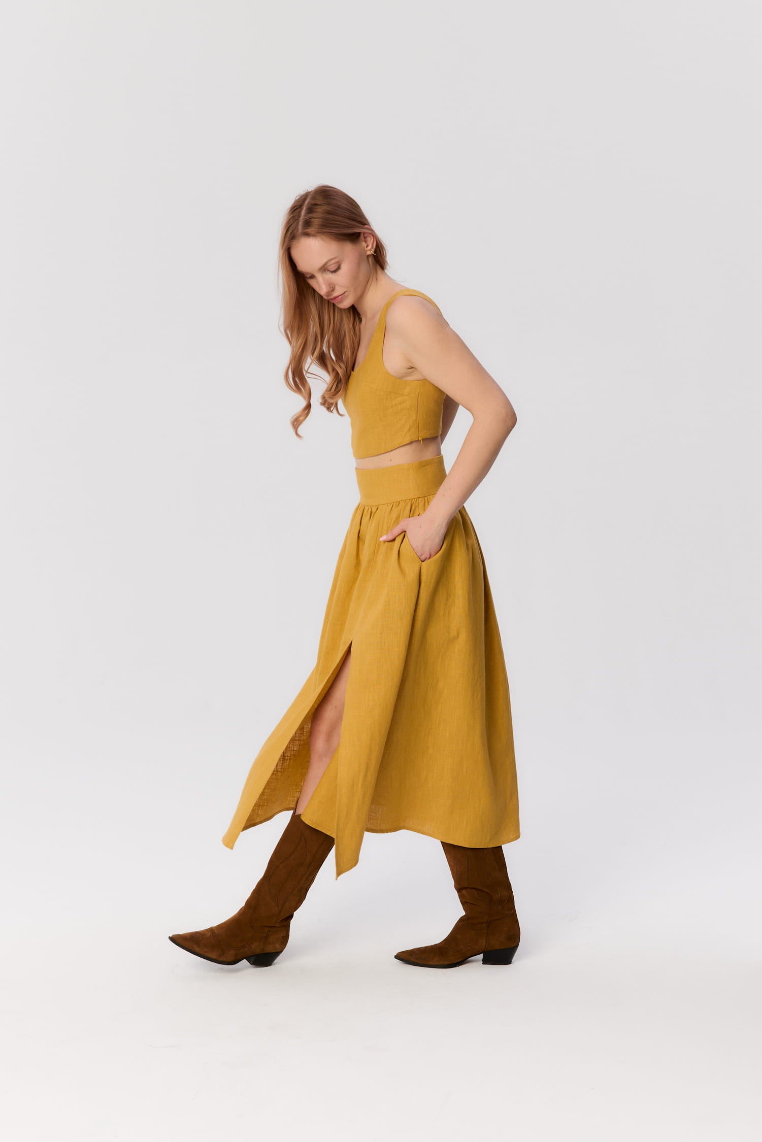 Modelka w ruchu w zestawie MAG NOLLY – topie Milo i spódnicy Sandrelli w kolorze ochry, z rozcięciem i brązowymi kowbojkami.