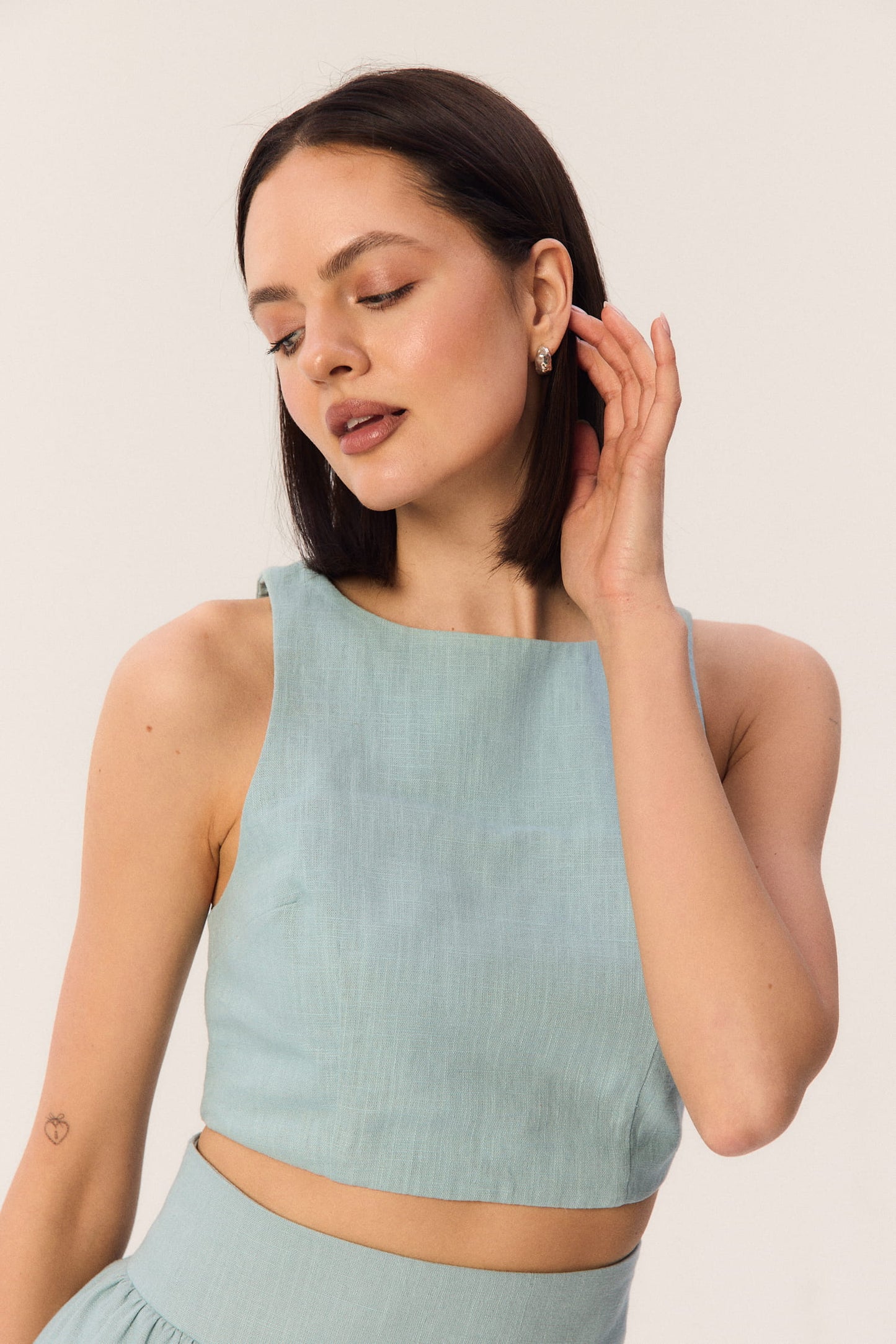 Zbliżenie na modelkę w turkusowym topie Loren bez rękawów z dekoltem pod szyję, kampanijne ujęcie.