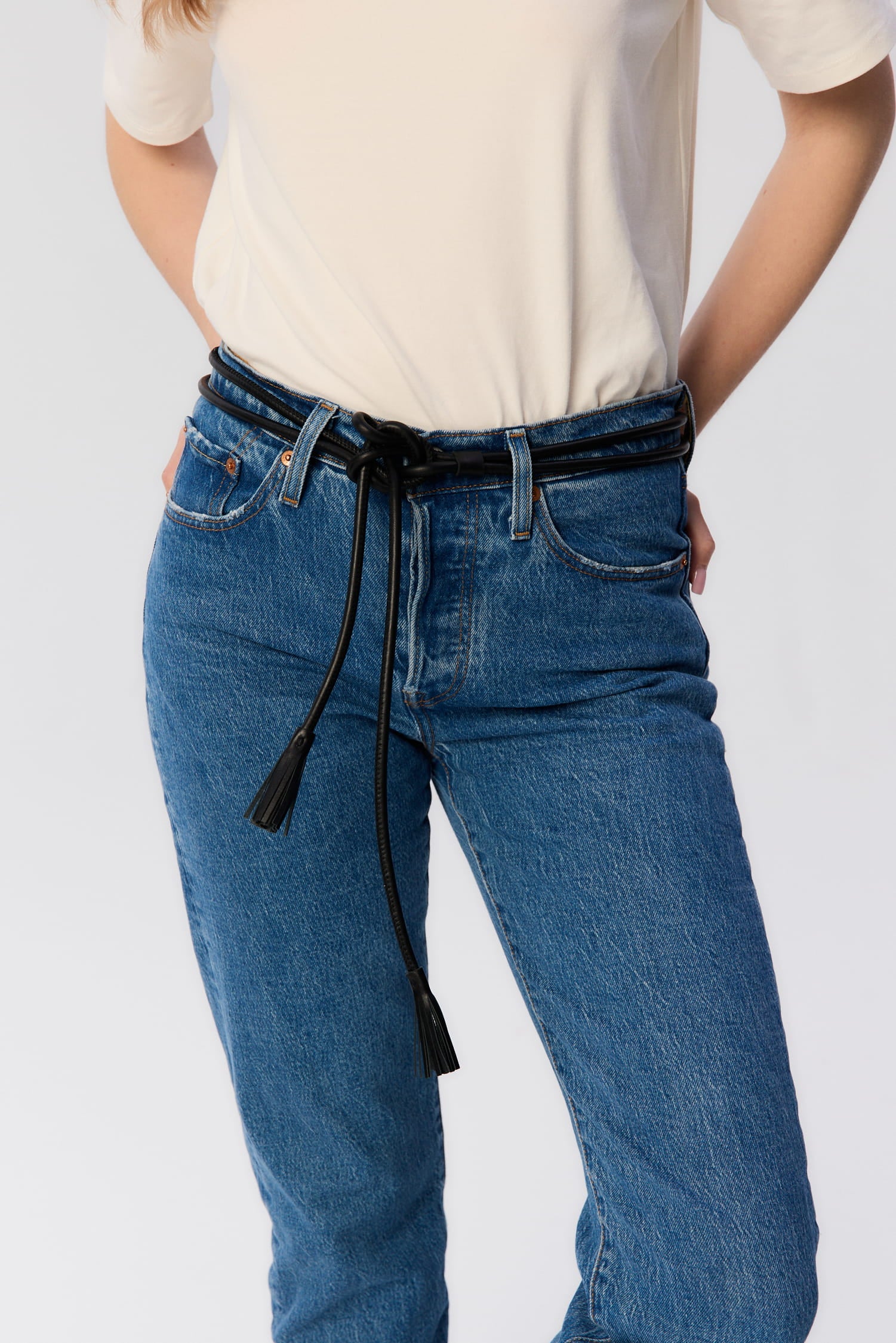 Pasek Renzi od MAG NOLLY – czarny rzemień z naturalnej skóry z chwostem, stylizacja z jeansami i kremowym topem.