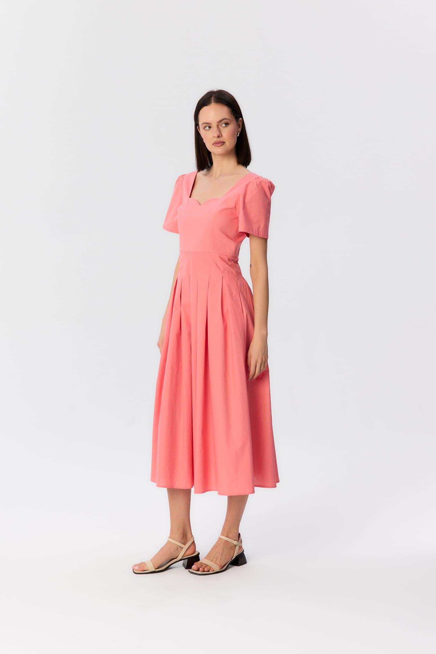 Modelka w koralowej sukience midi z krótkim rękawem i rzeźbiarskim dekoltem, projekt MAG NOLLY.