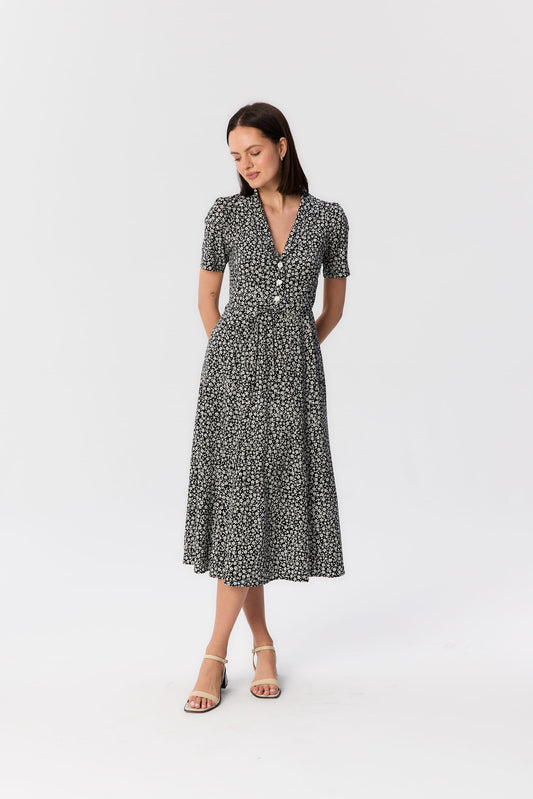 Modelka w czarno-białej sukience midi Bellucci z wiskozy, z krótkim rękawem, kołnierzykiem i drobnym kwiatowym wzorem, projekt MAG NOLLY.
