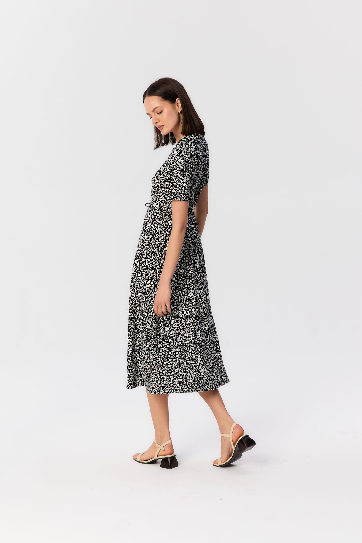 Modelka w sukience midi Bellucci od MAG NOLLY – czarno-biały kwiatowy wzór, krótki rękaw i kobieca sylwetka uchwycona z profilu.