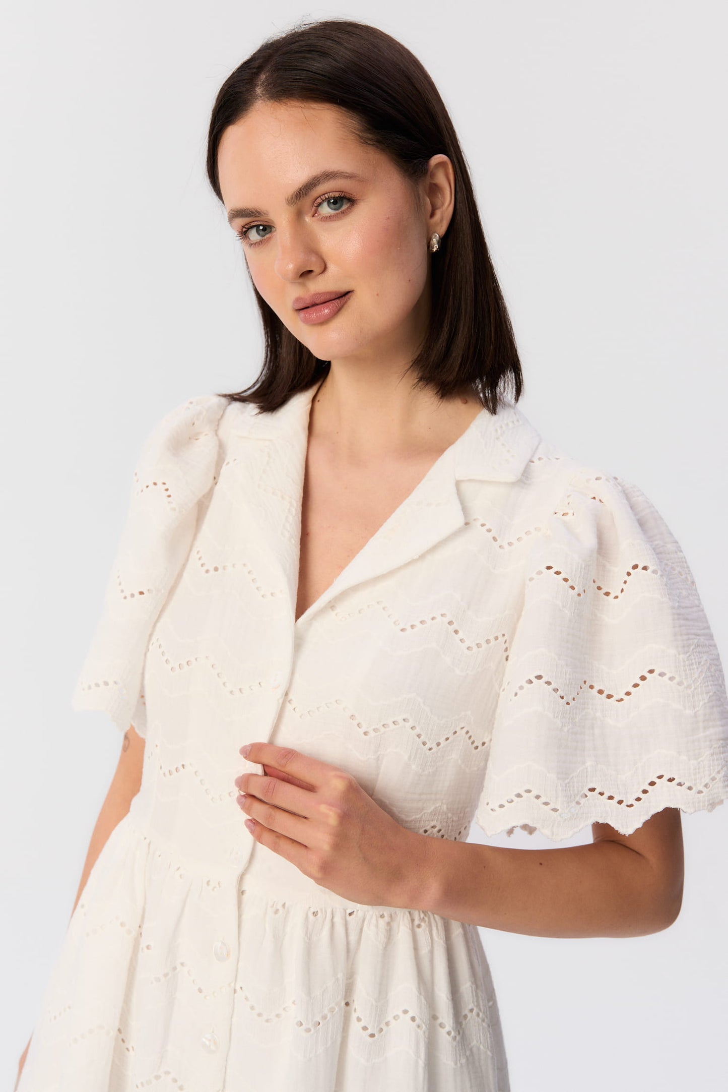 Zbliżenie na modelkę w sukience Duttonka z białego, haftowanego muślinu – kołnierzyk, bufiaste rękawy i lekki letni charakter projektu MAG NOLLY.