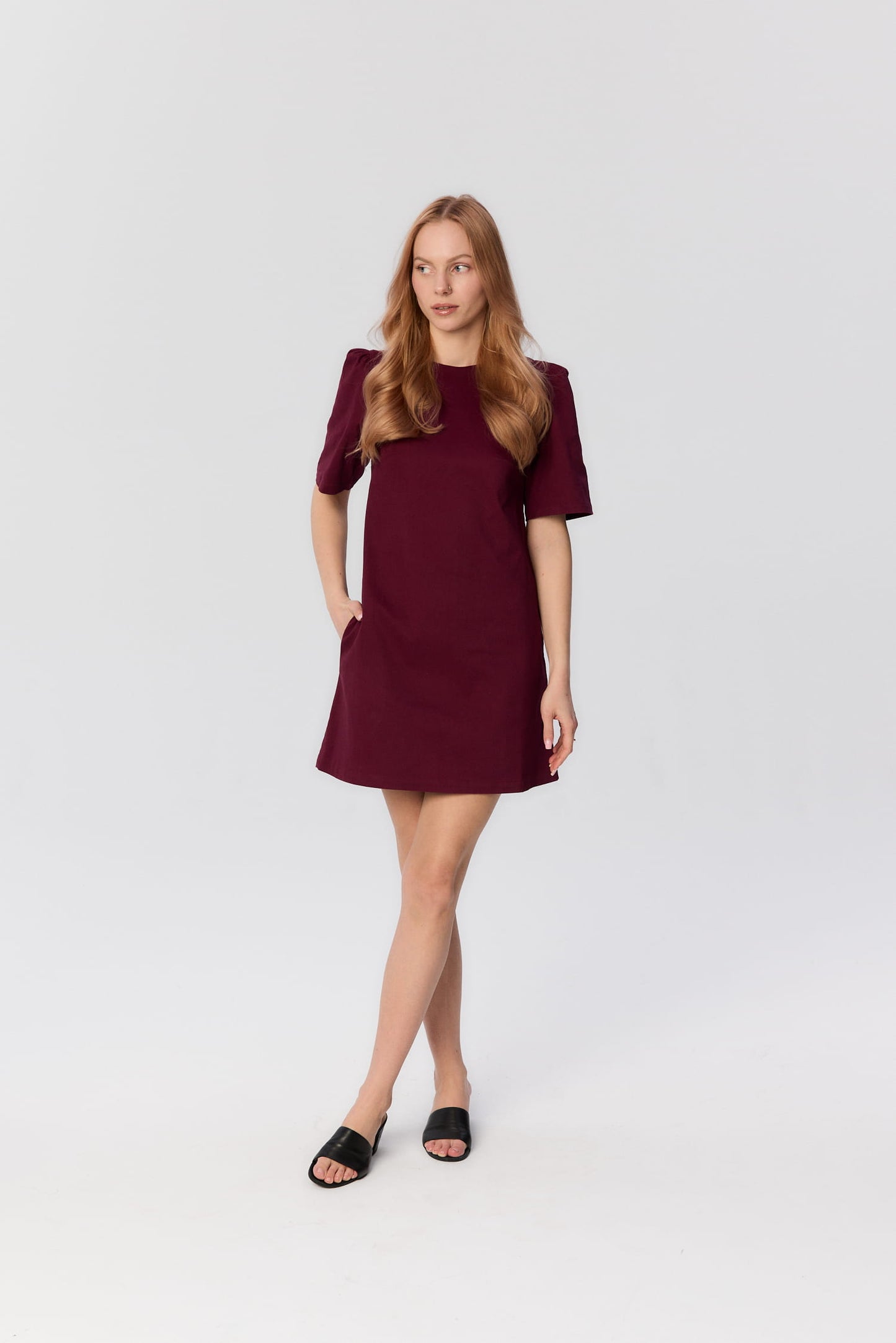 Modelka w krótkiej bordowej sukience Riva o trapezowym kroju – MAG NOLLY, widok całej sylwetki.