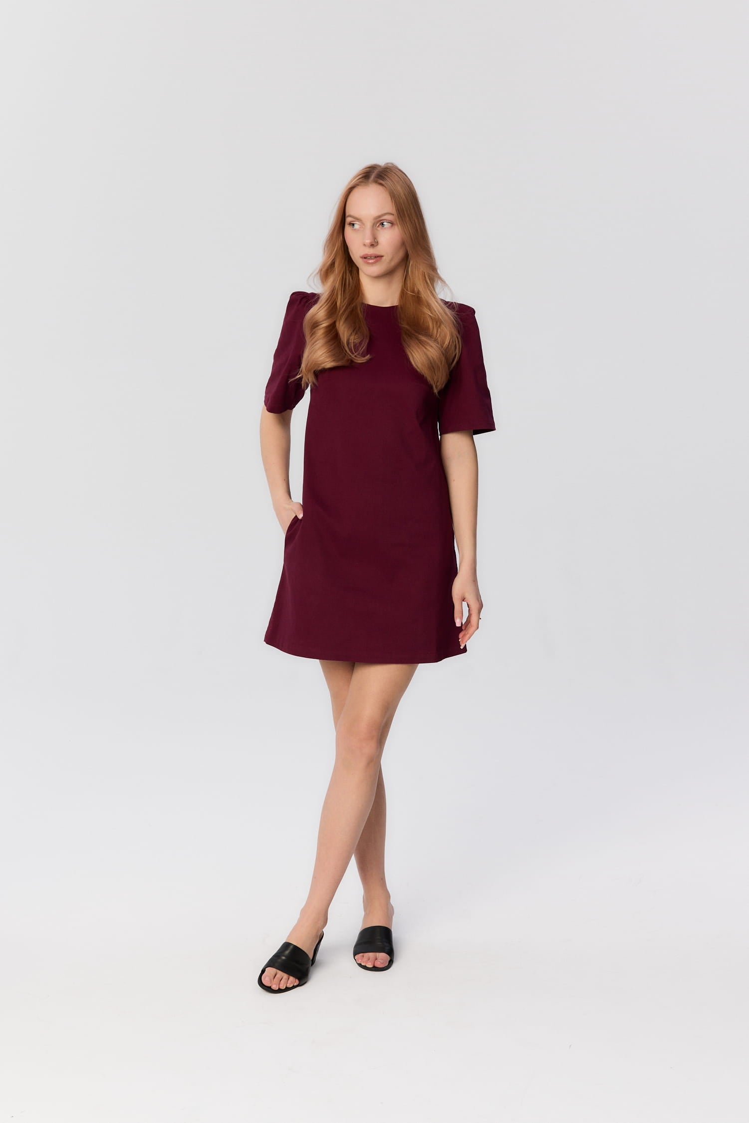 Modelka w krótkiej bordowej sukience Riva o trapezowym kroju – MAG NOLLY, widok całej sylwetki.