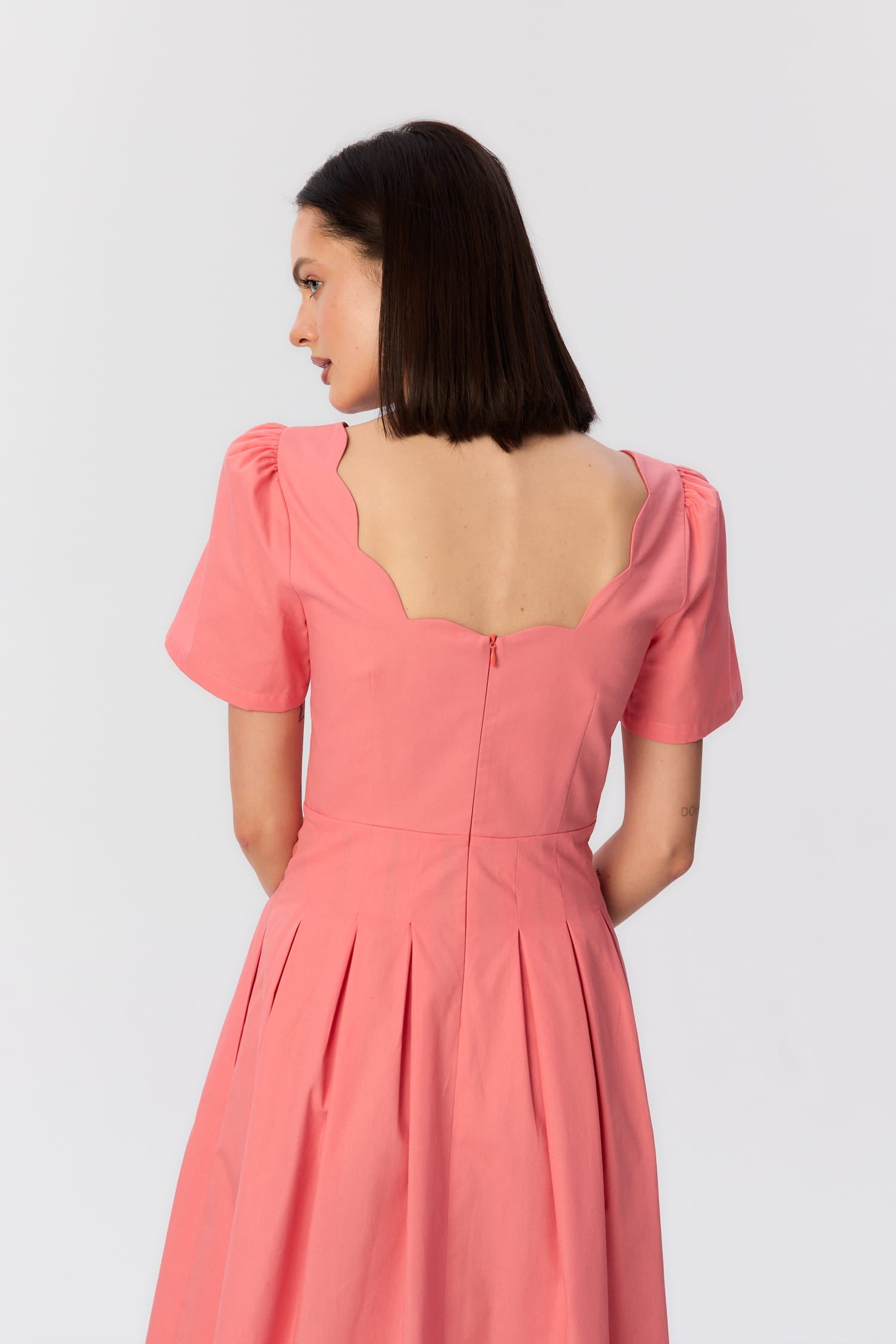 Zbliżenie na tył koralowej sukienki MAG NOLLY z falującym dekoltem i krótkim rękawem, elegancki detal kobiecej sylwetki.