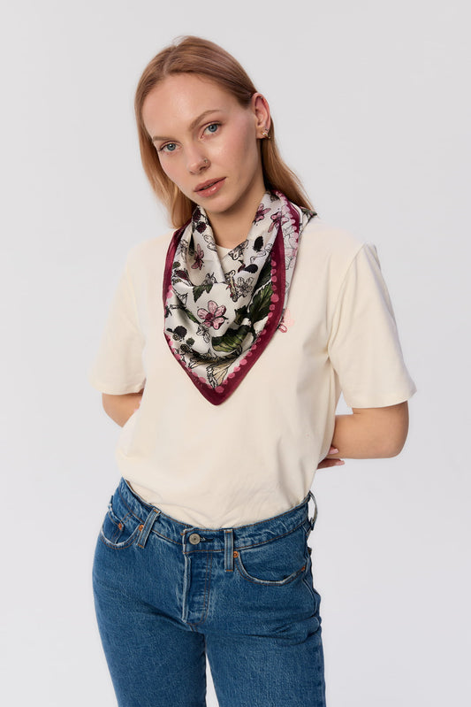 Modelka w białym t-shircie i dżinsach, z apaszką MAG NOLLY z jedwabiu we wzór jeżyn z bordową ramką, zawiązaną na szyi.
