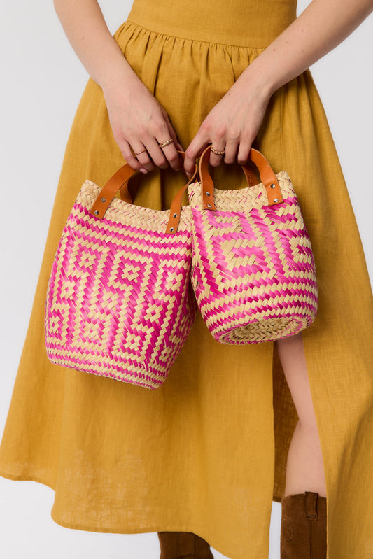Modelka trzyma dwa plecione koszyki Vitti w odcieniach różu – ręcznie wykonane z liści palmowych, z rączkami ze skóry naturalnej, w stylu boho.