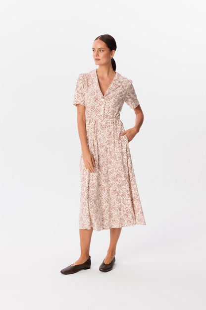 Sukienka Bellucci Rosella, midi z kołnierzykiem i krótkim rękawem, guziki z przodu, w jasny print w drobne plamki, modelka z ręką w kieszeni – MAG NOLLY