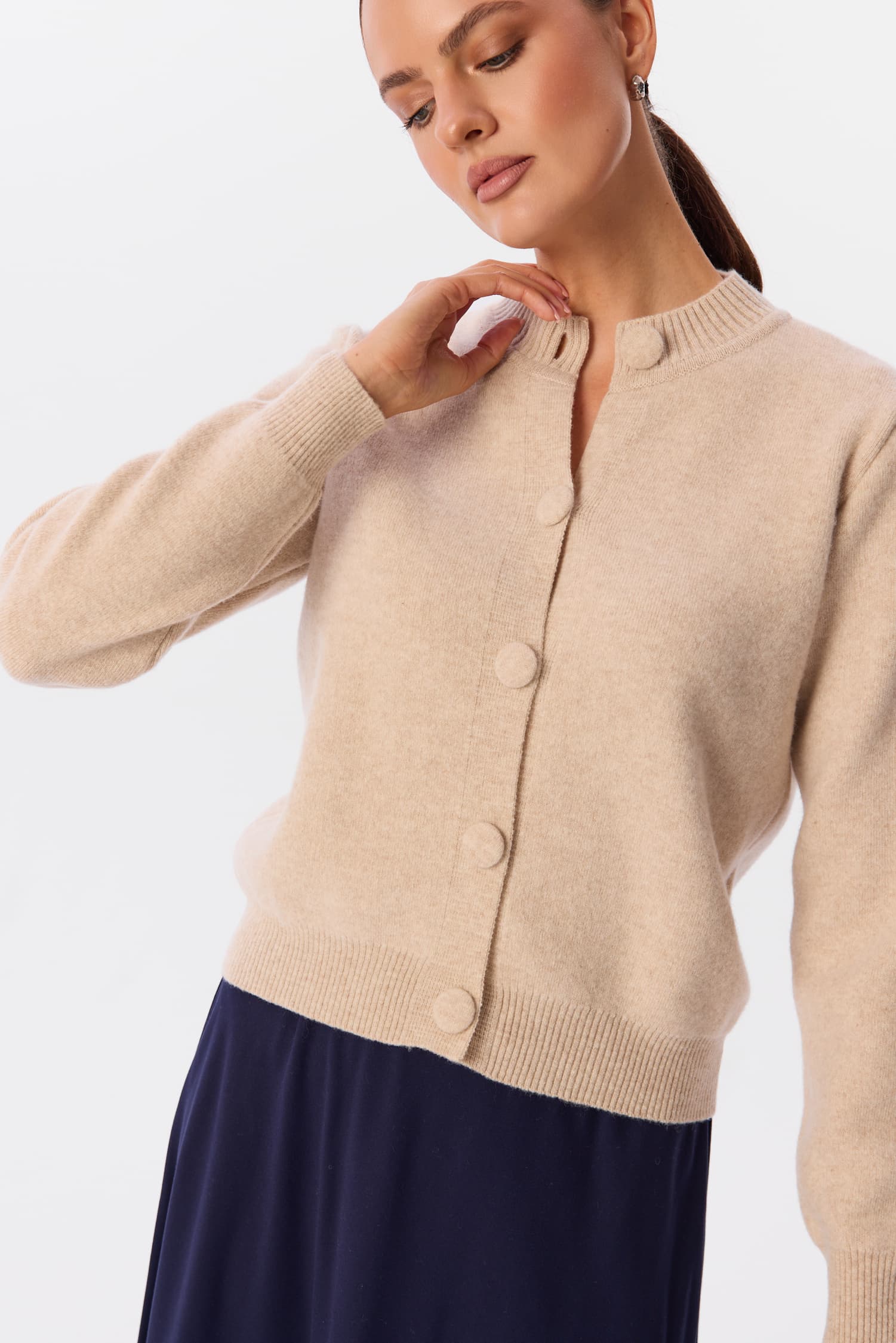 Sweter Livo w kolorze Soft Canvas, ujęcie detalu z przodu – modelka w beżowym kardiganie zapinanym na guziki, z prążkowanym wykończeniem pod szyją – MAG NOLLY