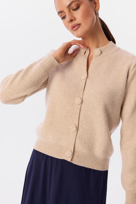 Sweter Livo w kolorze Soft Canvas, ujęcie detalu z przodu – modelka w beżowym kardiganie zapinanym na guziki, z prążkowanym wykończeniem pod szyją – MAG NOLLY