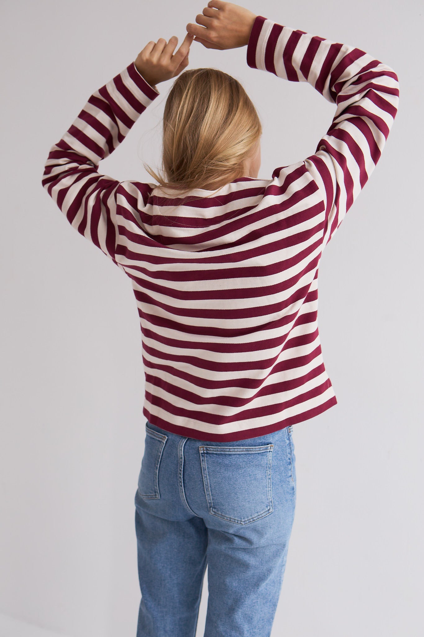 Bluzka Arla Mag Nolly – Bordeaux Milk, widok z tyłu, paski bordeaux i ecru, krój boxy, modelka z uniesionymi rękami, stylizacja z jeansami