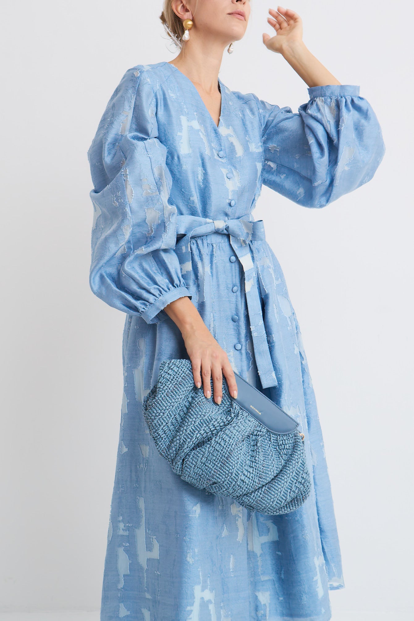 Sukienka Roma Mag Nolly – Blue Dust, zbliżenie na dekolt V, powlekane guziki, bufiaste rękawy z marszczonym mankietem, pasek w talii, faktura tkaniny